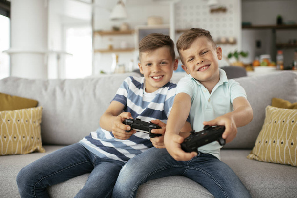 Hermanos felices jugando videojuegos. Los hermanos jóvenes se divierten mientras juegan videojuegos en la sala de estar. - Foto, imagen