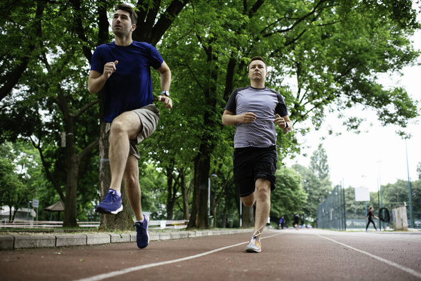Nuoret miehet treenaavat kilparadalla. Kaksi nuorta ystävää juoksemassa yleisurheiluradalla - Valokuva, kuva
