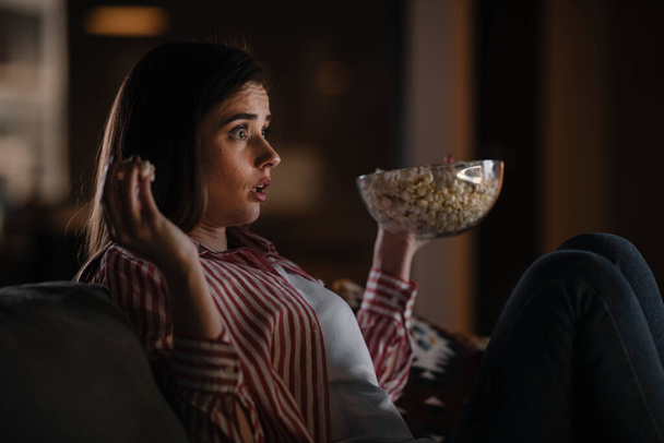 Όμορφη γυναίκα βλέποντας ταινία το βράδυ κάθεται σε έναν καναπέ στο σαλόνι στο σπίτι - Φωτογραφία, εικόνα