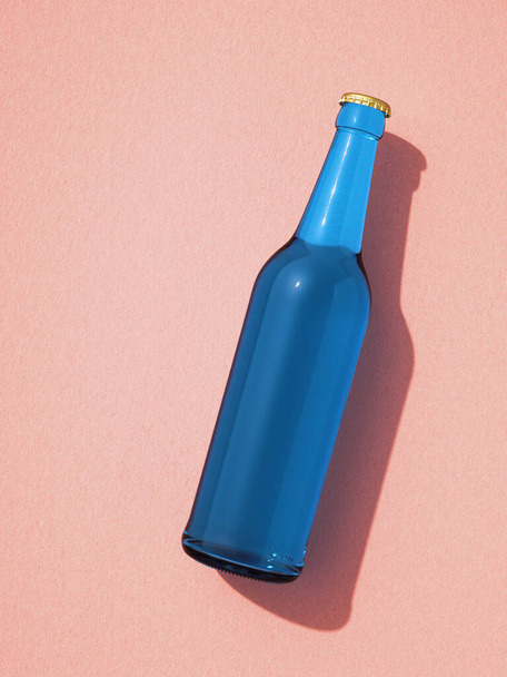 Single blue beer bottle laying on pink background. Mockup of glass bottle without label, shadow on background. Retro drink bottle concept. - Фото, изображение