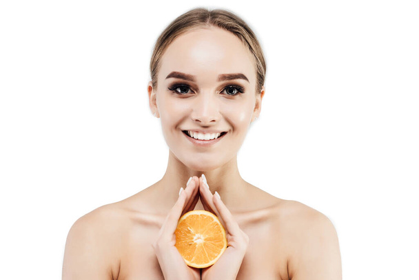 Portrait of a smiling beautiful girl with perfectly clean skin, she is holding an orange face and looking at the camera. Studio photo. Commercial photo. - Foto, Bild