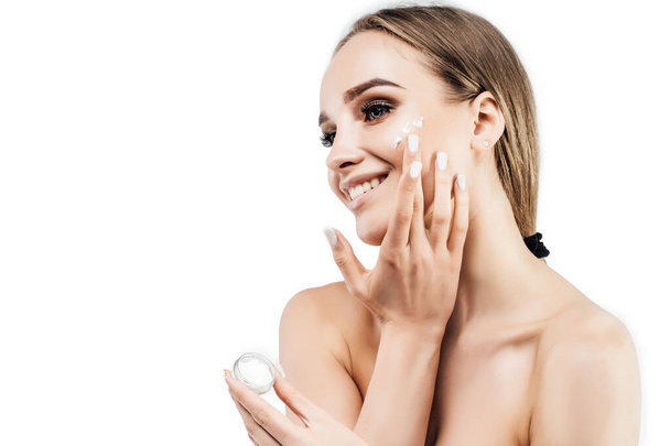 Portrait of a beautiful woman applying cream on her radiant and fresh face, she is on a white background with space for text. Gorgeous woman on a white background. Cosmetology, spa, beauty salon. - Photo, Image