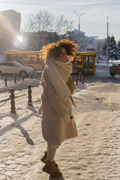 Young woman with dark curly hair, warmly dressed fur coat, scarf, winter frost, sunny day on the street in the city. - Foto, afbeelding