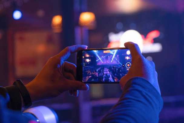 Ręce trzymające smartfona, aby zabrać VDO koncertu scenicznego z kolorowym oświetleniem laserowego światła reflektora show w dyskotekowym barze klubowym na spektakl festiwalu muzyki imprezowej. Nocne życie rozrywki. Zdarzenie. - Zdjęcie, obraz
