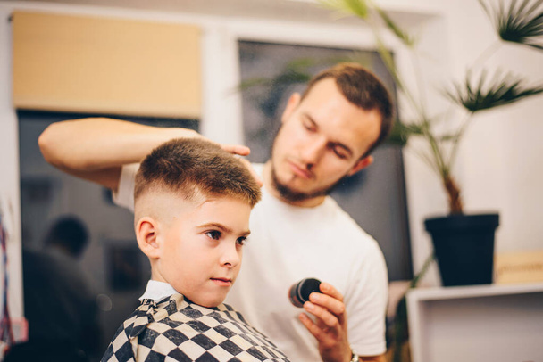 barber grooming cute little boy at hair salon - Foto, Imagen