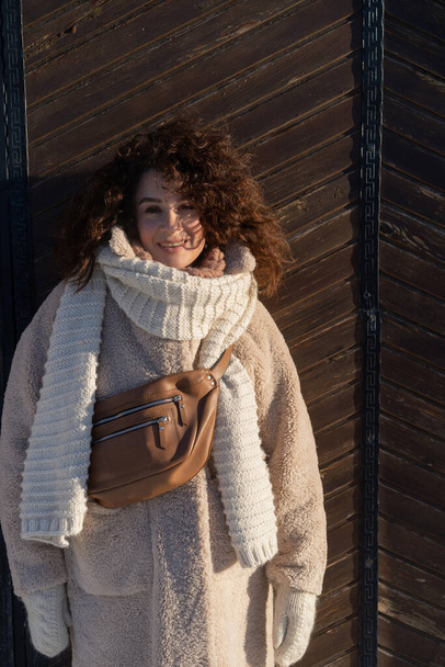 Young woman with dark curly hair, warmly dressed fur coat, scarf, winter frost, sunny day on the street in the city. - Foto, Bild
