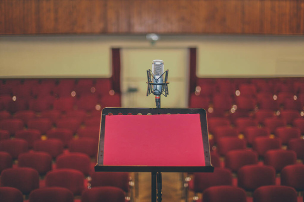 Notenständer oder Notenständer und ein altes Vintage-Mikrofon in einem kleinen Theater, Zuschauerraum oder einer Oper mit roten Plüschsitzen. - Foto, Bild