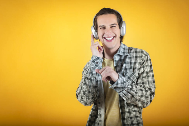 young guy listens to music in headphones happy, smiling, orange background - Φωτογραφία, εικόνα