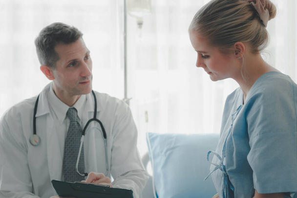 Young beautiful patient setting on the hospital bed, listening to the doctor to explain her health problems. Doctor doing a physical examination the patient and explaining, health care and hospital concept - Photo, Image
