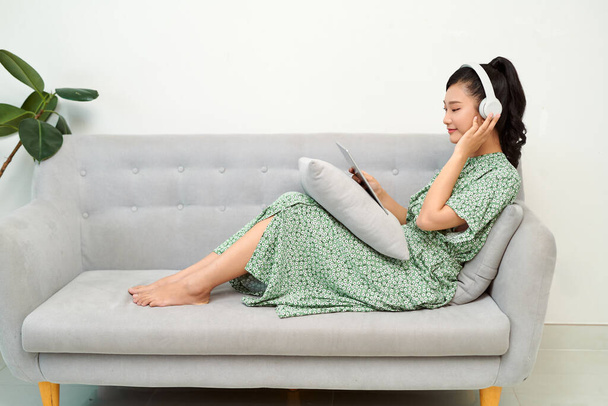 Souriant belle asiatique écouter de la musique tout en utilisant sa tablette dans le salon - Photo, image