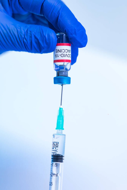 Lékař vpíchne jehlu injekční stříkačky do injekční lahvičky vakcínou COVID-19, aby extrahoval tekutinu k vakcinaci. Koncepce očkování proti koronaviru - Fotografie, Obrázek