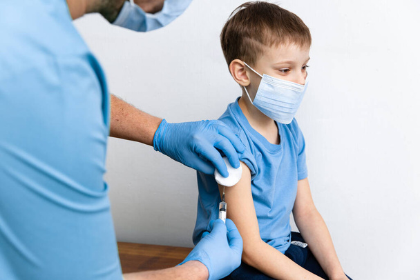 Vaccination concept. Male doctor vaccinating cute little boy in clinic, closeup. Vacctination session against coronavirus Covid-19 and immunity improvement - Foto, Imagen