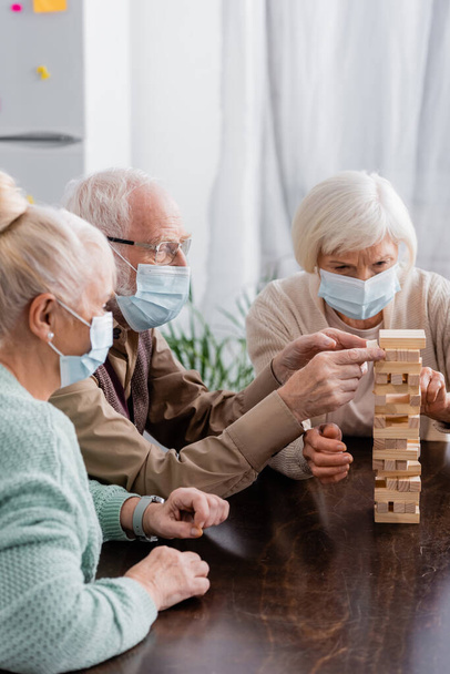 retired friends in medical masks playing tower wood blocks game at home - Фото, зображення