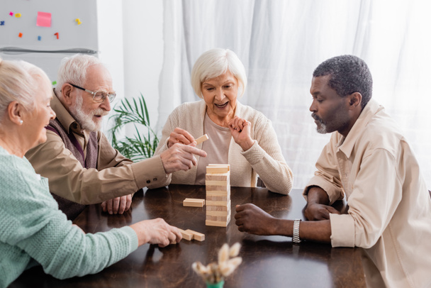 happy interracial pensioners playing tower wood blocks game at home - Foto, immagini