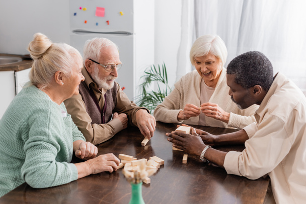 excited senior woman smiling while playing tower wood blocks game with interracial friends  - Foto, Imagem