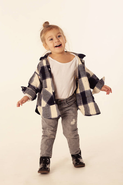 mignonne petite fille blonde en bottes noires, jeans, chemise à carreaux avec espace de copie isolé sur blanc - Photo, image