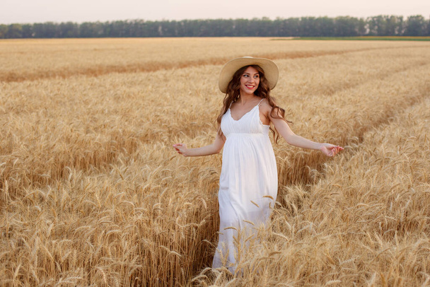 zwangere vrouw in een strohoed in een veld van tarwe - Foto, afbeelding