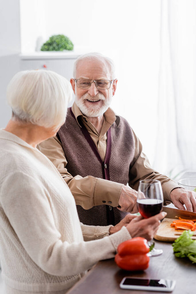 boldog idős férfi vágás paprika közelében felesége egy pohár bor - Fotó, kép