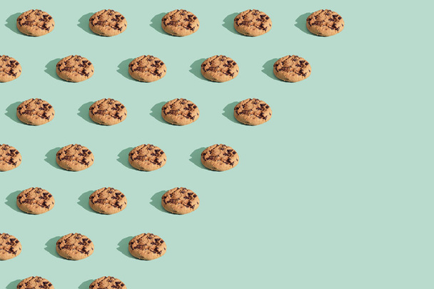 Trendy pattern made  of chocolate chip cookies on bright green mint background. Minimal concept, diagonal copy space. - Photo, Image
