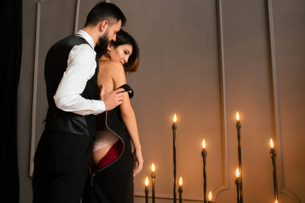 Portrait of a brutal beard man with tattoo  in hot elegant suit touches erotic sexy girl in sensual dress lingerie on loft apartment background . Couple love story concept - Фото, зображення
