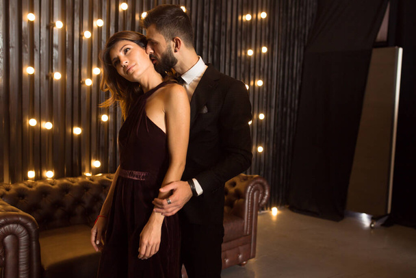 Portrait of a brutal beard man with tattoo  in hot elegant suit touches erotic sexy girl in sensual dress lingerie on loft apartment background . Couple love story concept - Fotografie, Obrázek
