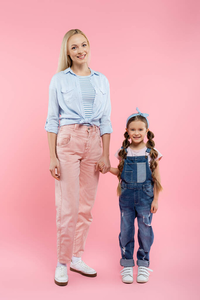 full length of happy mother and daughter holding hands and standing on pink - Foto, Bild