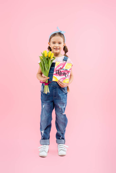 pleine longueur de gamin heureux tenant des tulipes et une carte de vœux avec je t'aime maman lettrage sur rose  - Photo, image