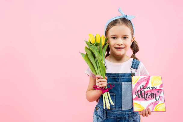 Веселый ребенок держит тюльпаны и открытки с я люблю тебя мама буквы изолированы на розовый  - Фото, изображение