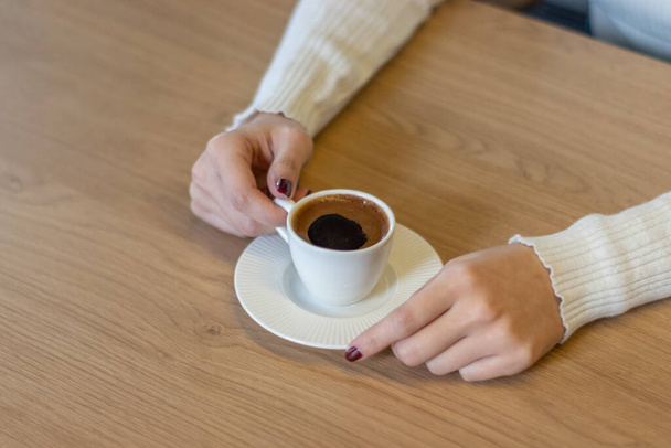 Η γυναίκα στο ξύλινο τραπέζι κρατώντας τούρκικο καφέ με τα χέρια σας - Φωτογραφία, εικόνα