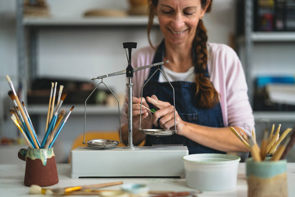 Donna felice versando vernice colori polvere su equilibrio vintage in studio di ceramica - Focus sull'equilibrio - Foto, immagini