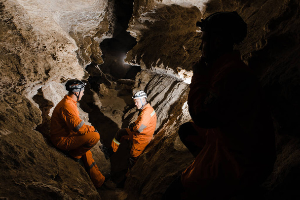 Drei Männer von kräftiger Statur erkunden die Höhle. Männer in Spezialkleidung gingen durch die Höhle und blieben stehen, schauten auf die Karte. - Foto, Bild