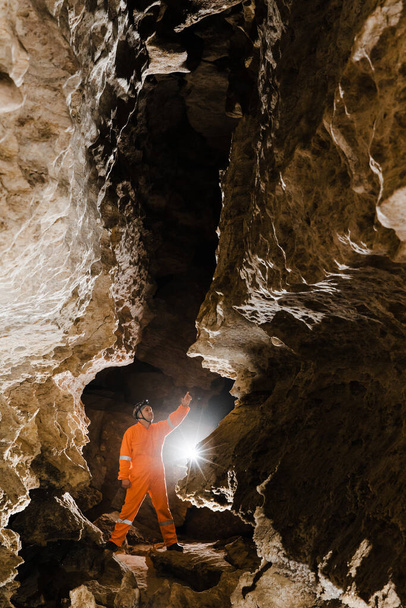 Hombre caminando y explorando cueva oscura con faro de luz bajo tierra. - Foto, imagen