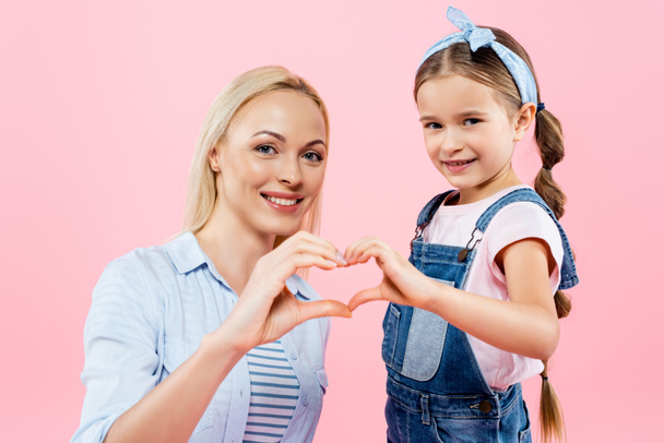 ευτυχισμένη μητέρα και κόρη δείχνουν σημάδι καρδιάς με τα χέρια απομονώνονται σε ροζ - Φωτογραφία, εικόνα