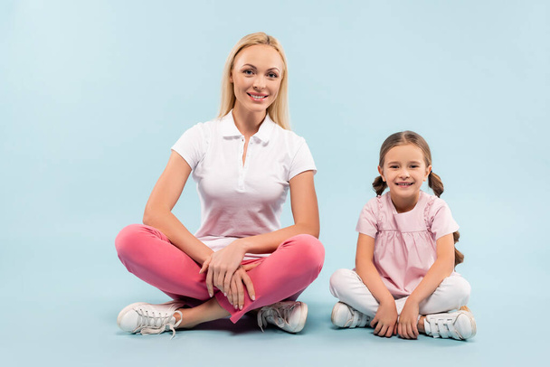 happy mother and child sitting with crossed legs on blue background - Photo, Image