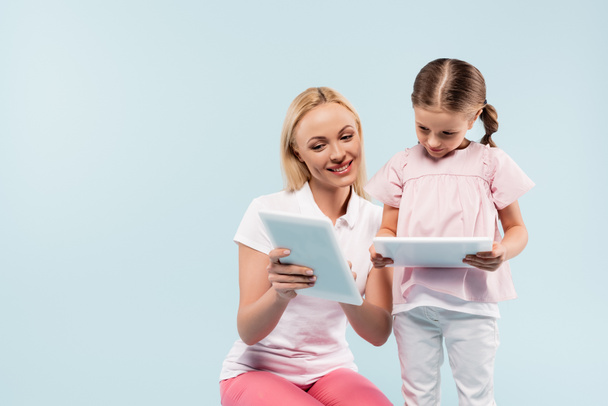 happy mother and daughter holding digital tablets isolated on blue - Фото, зображення