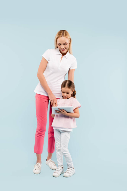 full length of happy mother and daughter looking at digital tablet on blue - Foto, imagen