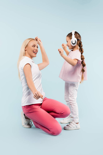 szczęśliwy dzieciak w słuchawkach bezprzewodowych taniec z matką na niebiesko - Zdjęcie, obraz