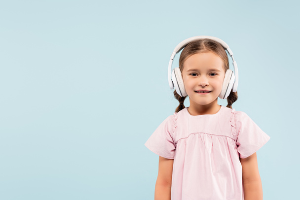 happy kid in wireless headphones smiling isolated on blue - Photo, Image