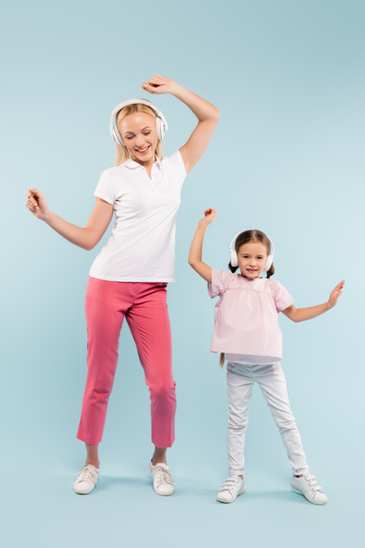 full length of cheerful mother and kid in wireless headphones dancing on blue - Φωτογραφία, εικόνα