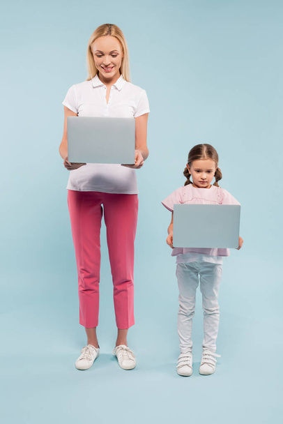 full length of mother and daughter standing with laptops on blue - Fotografie, Obrázek