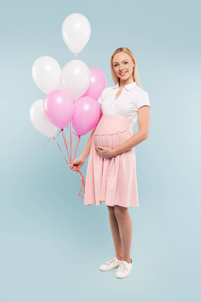 full length of pregnant woman holding balloons on blue - Foto, Imagem
