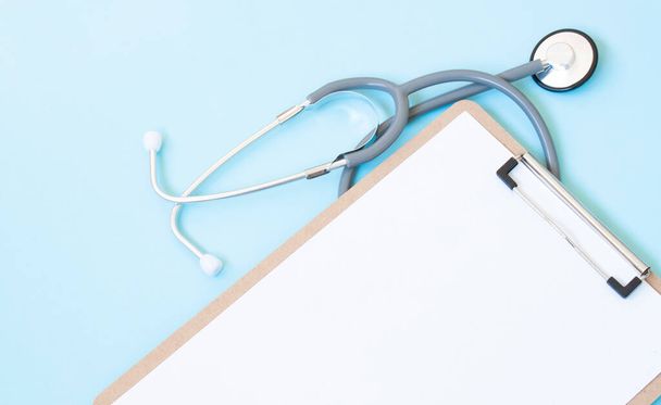 A wooden clipboard and stethoscope with white paper on it, set against a blue background - Фото, зображення