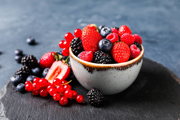 Bowl with different ripe berries on dark background - Photo, Image