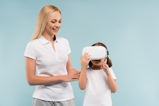 cheerful mother looking at daughter in vr headset isolated on blue - Фото, зображення