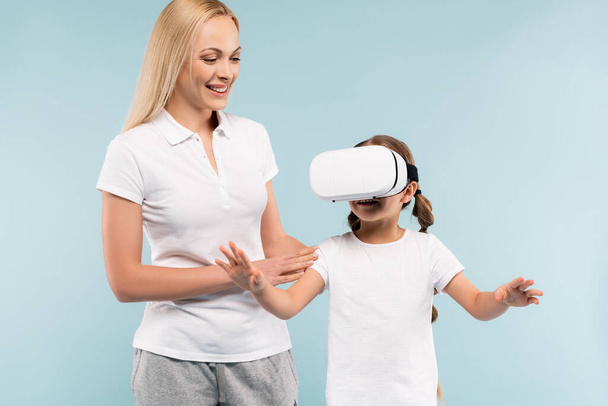 cheerful mother smiling near daughter in vr headset isolated on blue - Фото, зображення