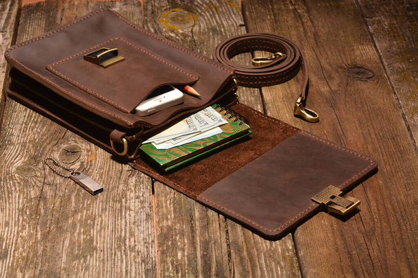 Un sac, de l'argent, un smartphone, un ordinateur portable et une clé USB dans un sac ouvert en cuir marron, accessoires pour hommes - Photo, image