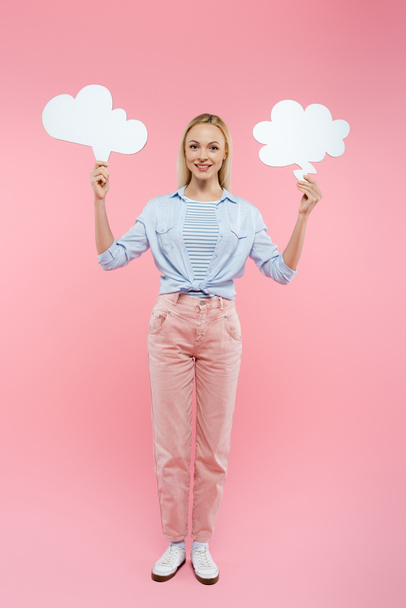 full length of cheerful blonde woman holding thought bubbles on pink  - Foto, afbeelding