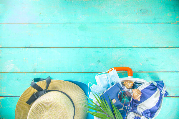 Strand és nyaralás Nyaralás kiegészítők Blue Plank. Bőrönd utazáshoz, nyári női ruházat, napszemüveg, kiegészítők és trópusi levelek élénk kék háttérrel másolás helyet szöveg tetejére nézet - Fotó, kép