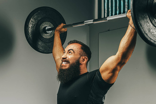 Muscular man in black sportswear lifting barbell in a gym - Фото, зображення