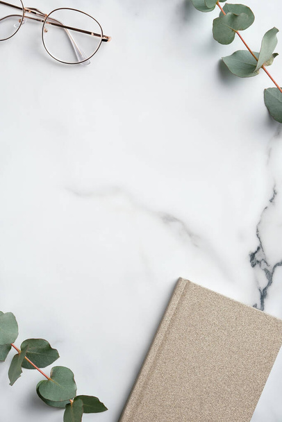 Creative workspace with paper notebook, glasses, eucalyptus leaves on marble background. Minimal style home office desk table. Flat lay, top view. - Fotoğraf, Görsel